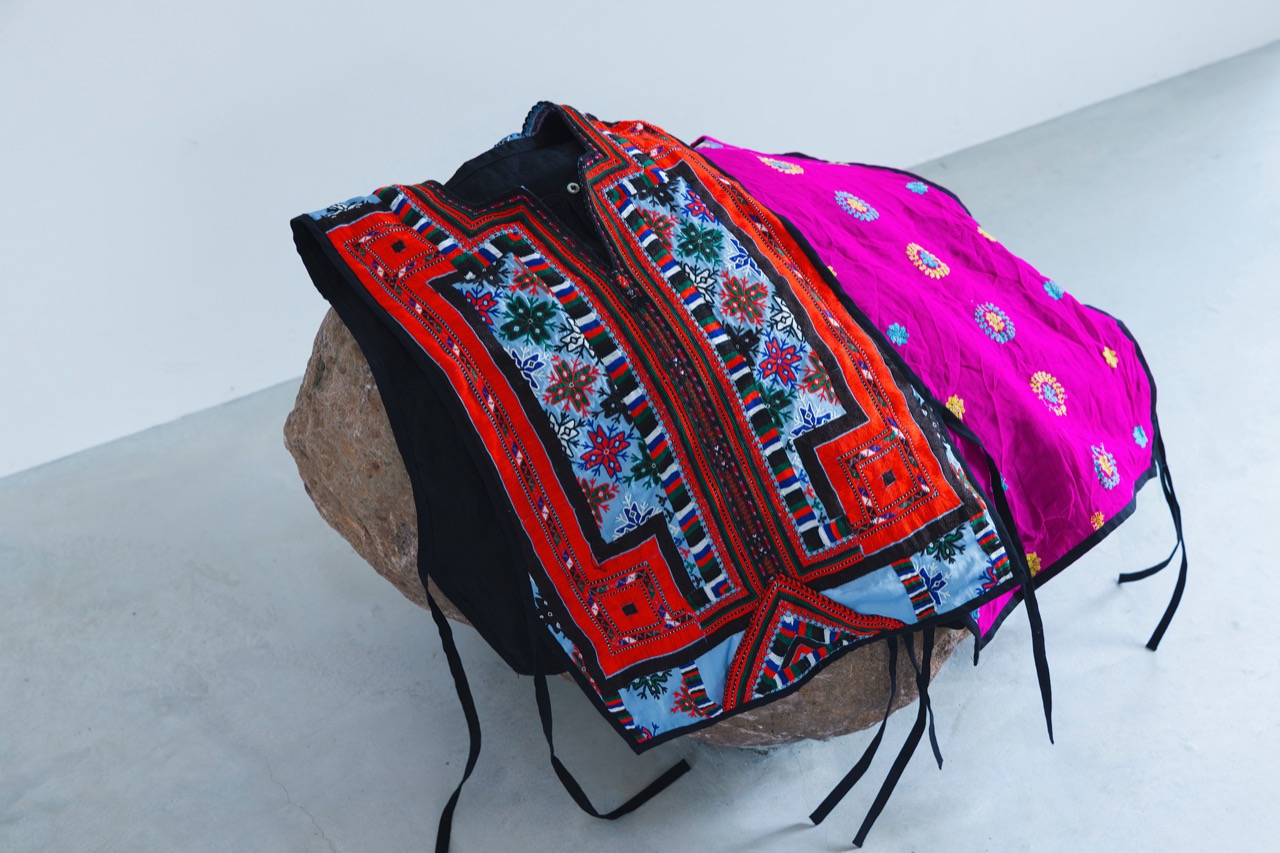 石の上に置かれた、色鮮やかな刺繍の民族衣装とピンクの布
