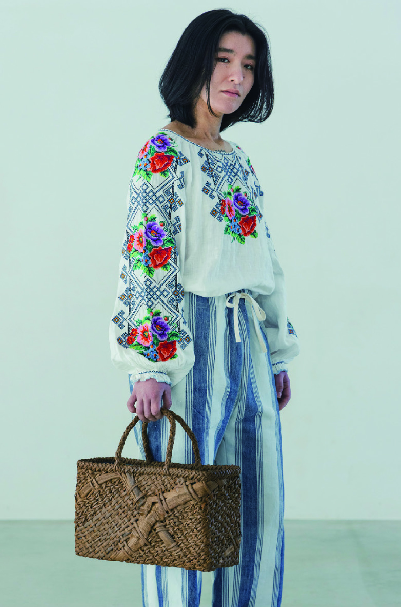 花刺繍のブラウスとストライプパンツに籠バッグを合わせた女性